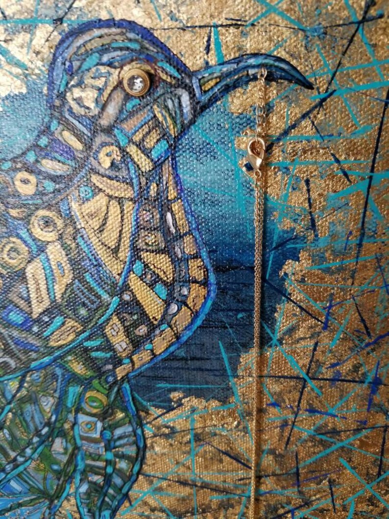 May include: An abstract painting of a bird in shades of blue, gold, and teal. The bird has a detailed mosaic-like pattern. A delicate gold chain with a charm hangs from the bird's beak. The background is a mix of gold and blue.