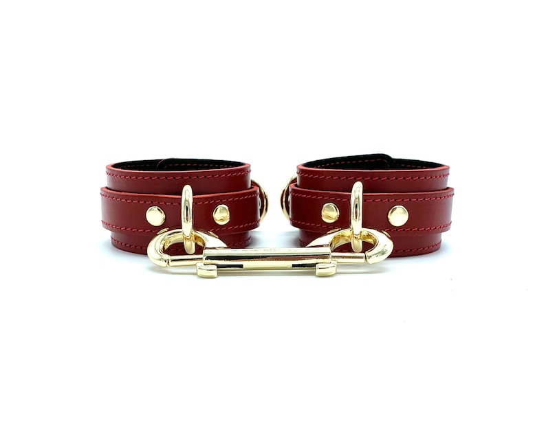 May include: A pair of red leather wrist cuffs with gold metal accents and a connecting clasp.
