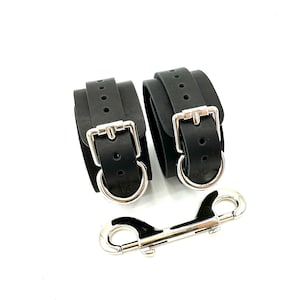 May include: A pair of black leather wrist cuffs with silver metal buckles and a silver metal connecting hook.