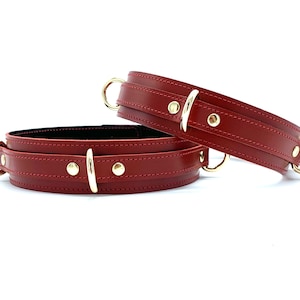 May include: Two red leather restraints with gold metal buckles and rings.