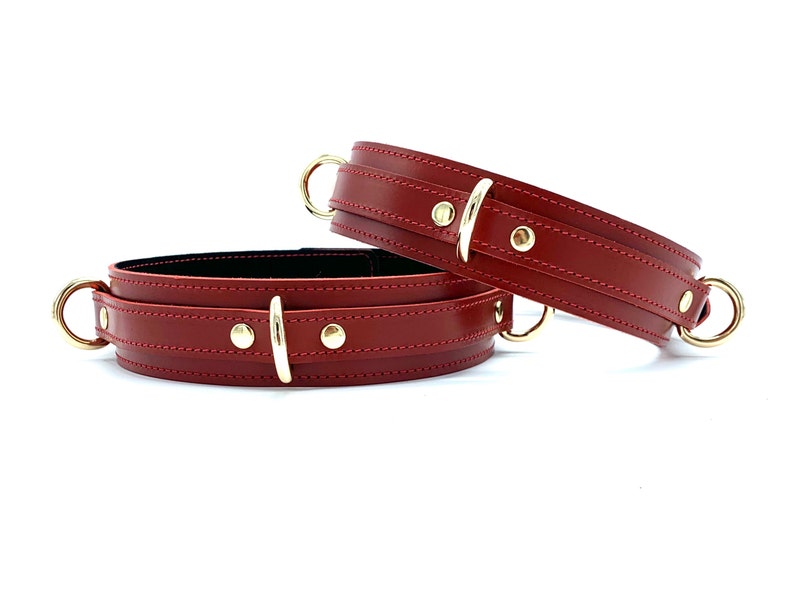 May include: Two red leather restraints with gold metal buckles and rings.