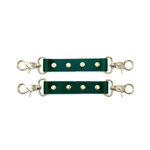 May include: Two green leather straps with gold metal clasps and gold studs. Each strap has five gold studs.