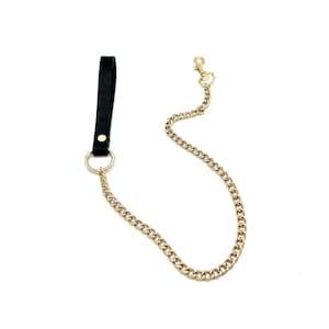 May include: A black leather strap with a gold-colored metal ring and a gold-colored chain. The chain has a lobster clasp at the end. The strap is attached to the ring with a gold-colored rivet.