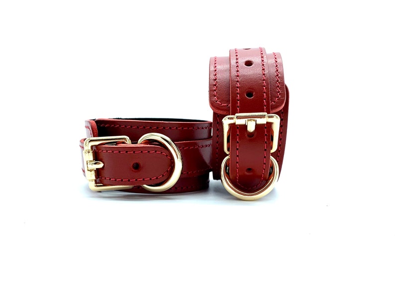 May include: A pair of red leather wrist cuffs with gold metal buckles and D-rings.