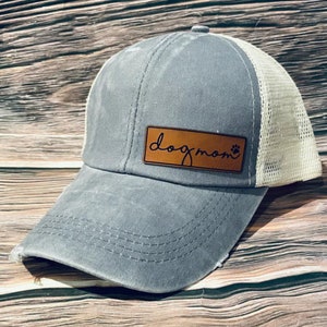 May include: A blue and white trucker hat with a brown leather patch that says "dog mom" with a paw print.
