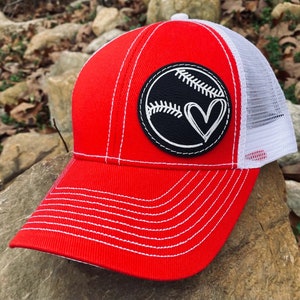 Könnte beinhalten: Rote und weiße Baseballkappe mit einem schwarzen Lederpatch, auf dem ein Baseball mit einem Herz darin abgebildet ist. Der Patch hat weiße Nähte an den Rändern.
