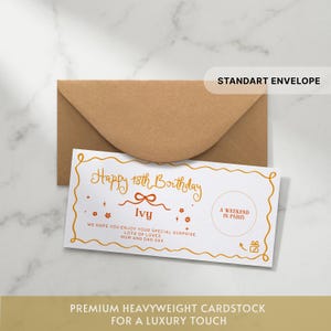 May include: A white rectangular gift voucher with a wavy orange border, featuring the text Happy 18th Birthday Ivy, A WEEKEND IN PARIS, and a message from Mum and Dad. The voucher is placed in front of a brown kraft paper envelope.