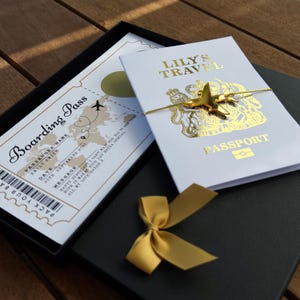 May include: A white boarding pass with a world map and text including Boarding Pass, Passenger Name Emily Smith, and Date 25th September 2027, alongside a white passport cover titled Lily's Travel with a gold airplane charm and a gold ribbon.