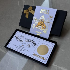 May include: A black gift box containing a white card with gold foil text reading Emily's Driving Journey and a gold key charm. A second black box holds a white voucher with the text Driving Lessons, a scratch-off circle, and car graphics.