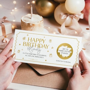 May include: A birthday gift card with gold text reading "Happy Birthday Emily". The card features a scratch-off section with "Off to Harry Potter Studios!". A small cake with a candle is in the background, along with balloons.