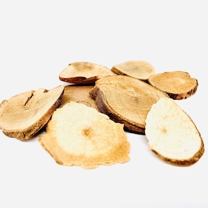 May include: Close-up of dried slices of a light brown root, likely a medicinal herb, on a white background.