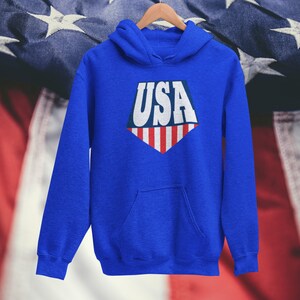 May include: A royal blue hoodie with a white, red, and blue USA graphic on the front. The graphic is a diamond shape with the word "USA" in white letters and red and white stripes at the bottom.