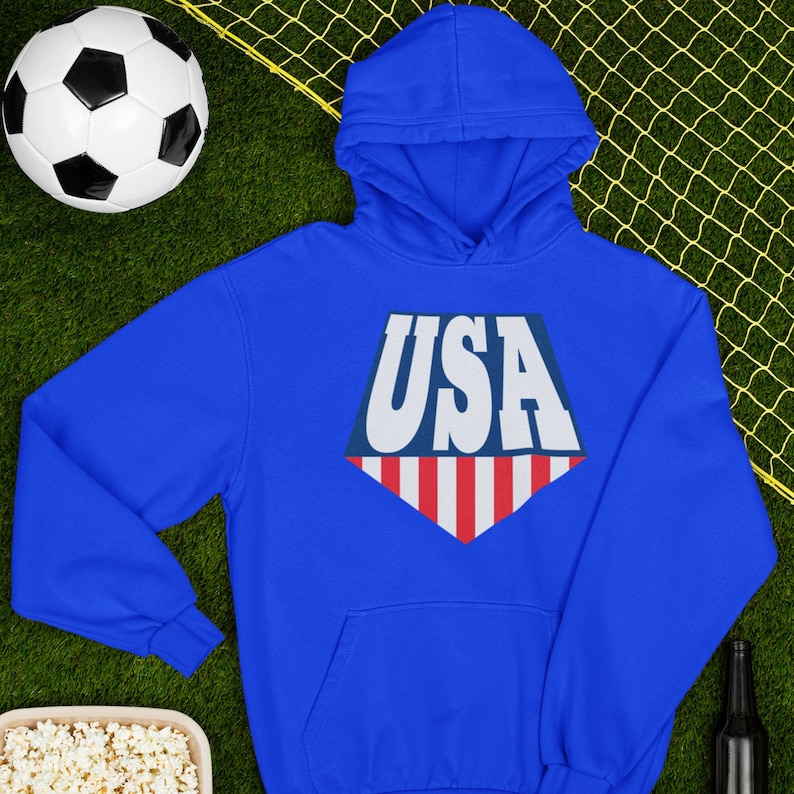 May include: A royal blue hooded sweatshirt with a white, red, and blue USA graphic on the front. The graphic is in the shape of a diamond with the word "USA" in white letters on a blue background and red and white stripes at the bottom.