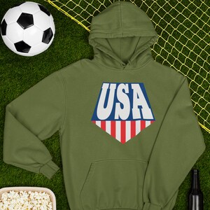 May include: A green hooded sweatshirt with a white, blue, and red USA graphic on the front. The graphic is in the shape of a diamond with a red and white striped bottom.