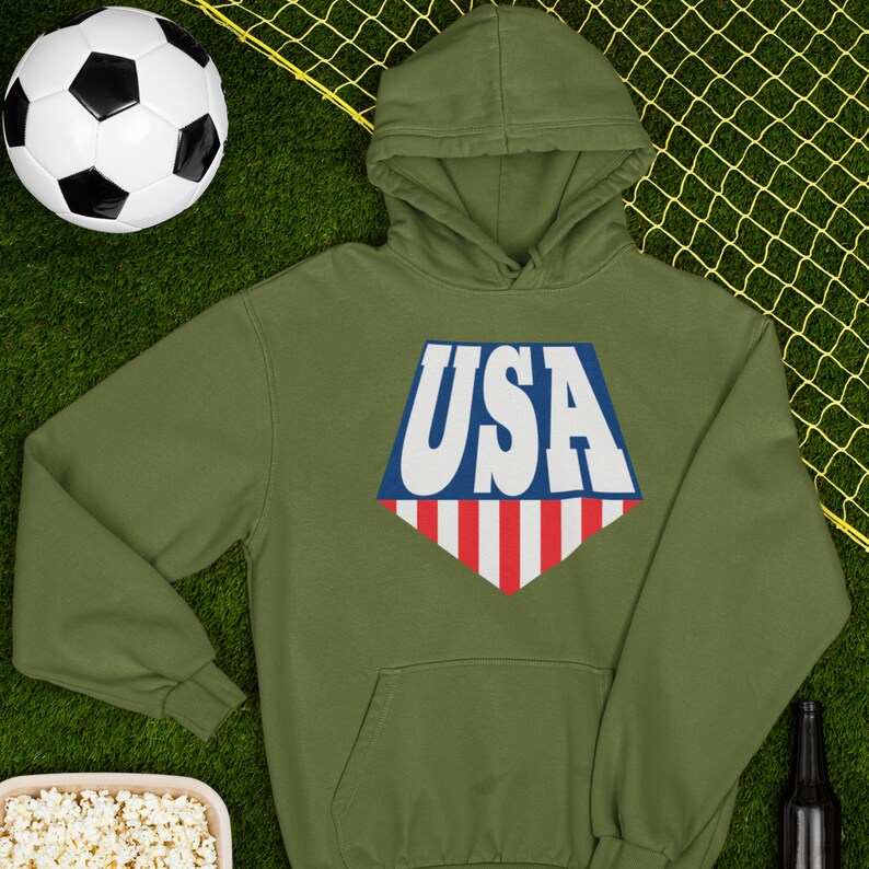 May include: A green hooded sweatshirt with a white, blue, and red USA graphic on the front. The graphic is in the shape of a diamond with a red and white striped bottom.