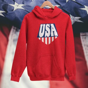 May include: Red hooded sweatshirt with a white and blue graphic of the word "USA" in a shield shape with stripes.
