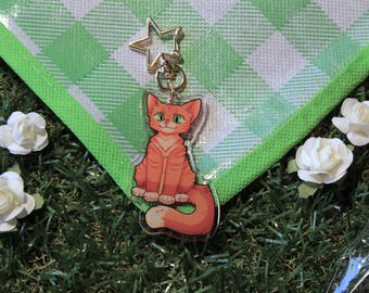 May include: Orange tabby cat cartoon character charm with a star charm attached to a gold chain. The charm is on a green and white checkered background.