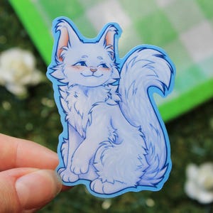 May include: A white cat sticker with blue outlines. The cat is sitting with its tail curled around its body. The cat has a happy expression on its face.