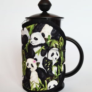 May include: Black and white panda design insulated coffee press cosy. The cosy is made of fabric with a black background and a pattern of pandas and bamboo.