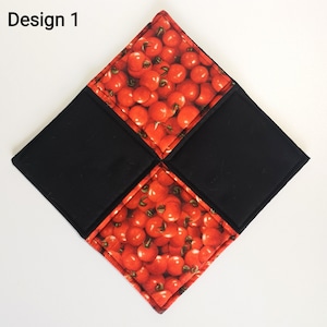 May include: A square, quilted hot pad with a design featuring red tomatoes and black fabric. The hot pad is divided into four diamond shapes, with the tomatoes printed on two opposite diamonds and black fabric on the other two.