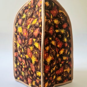 May include: A brown quilted fabric cover with a tan trim. The fabric has a pattern of yellow and orange fireworks on a dark brown background.