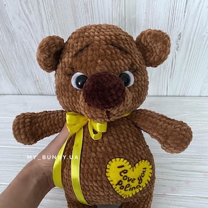 May include: A brown crocheted teddy bear with a yellow ribbon around its neck. The bear has a heart-shaped patch on its chest that says "I love you Polina".