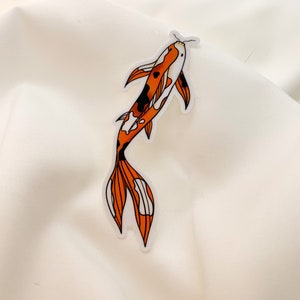 May include: A sticker depicting a koi carp. The fish is coloured orange, black, and white, with black outlines. The sticker is set against a white backdrop.