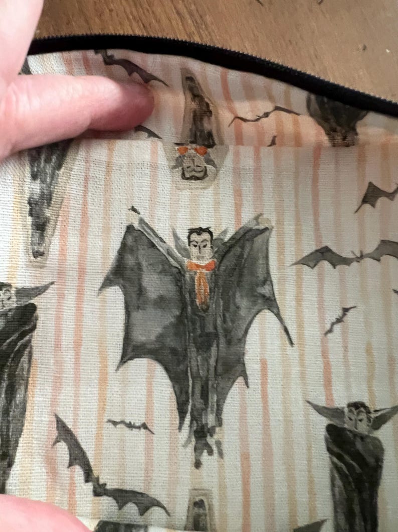 K&ouml;nnte beinhalten: Nahaufnahme eines Halloween-Stoffs mit einem sich wiederholenden Muster aus Aquarell-Vampiren und Flederm&auml;usen. Die Vampire haben dunkle Umh&auml;nge und orangefarbene Fliegen. Der Hintergrund hat vertikale Pfirsichstreifen.