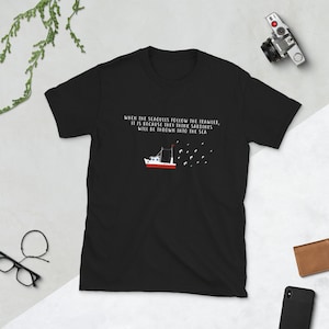 以下が含まれることがあります： 赤い漁船とカモメの白いグラフィックが描かれた黒いTシャツ。テキストは「WHEN THE SEAGULLS FOLLOW THE TRAWLER, IT IS BECAUSE THEY THINK SARDINES WILL BE THROWN INTO THE SEA.」です。
