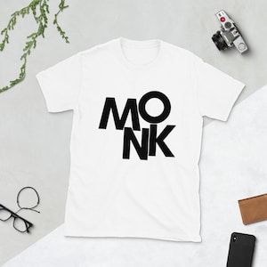 Puede incluir: Camiseta blanca con un diseño gráfico negro que dice "MONK" en una fuente negrita y estilizada.