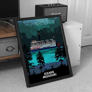 May include: A black framed print of a riverboat casino with the text "MISSOURI BELLE" and "CASINO" on the side of the boat. The boat is on a body of water with trees in the background. The text "OZARK MISSOURI" is at the bottom of the print.