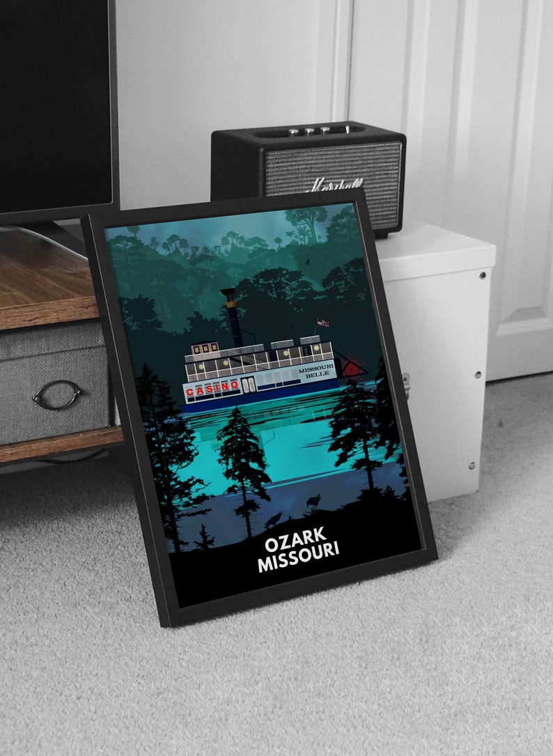 May include: A black framed print of a riverboat casino with the text "MISSOURI BELLE" and "CASINO" on the side of the boat. The boat is on a body of water with trees in the background. The text "OZARK MISSOURI" is at the bottom of the print.