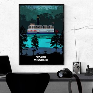 May include: A black framed poster with a blue and white illustration of a riverboat with the text "CASINO" on the side. The boat is on a body of water with trees in the background. The text "OZARK MISSOURI" is at the bottom of the poster.