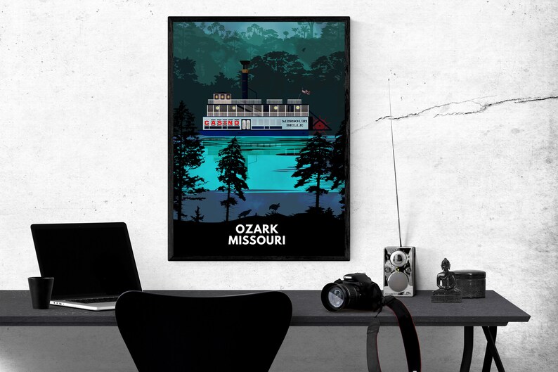 May include: A black framed poster with a blue and white illustration of a riverboat with the text "CASINO" on the side. The boat is on a body of water with trees in the background. The text "OZARK MISSOURI" is at the bottom of the poster.