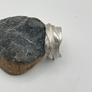 Puede incluir: Una taza de cerámica blanca con un asa negra y el texto "But First, Coffee" en un estilo manuscrito. La taza está sobre una superficie blanca. La taza mide 10 cm de alto.