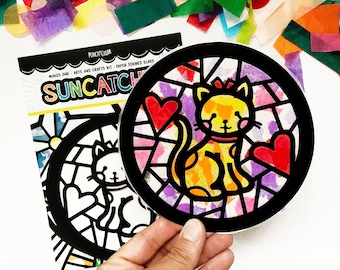 May include: A black and white outline of a cat with hearts, ready to be decorated with colorful tissue paper for a suncatcher craft project. The kit is called "Suncatch" and is made by Punch Color.