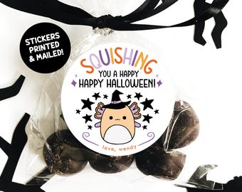 May include: A round sticker with a purple, orange, and white axolotl wearing a witch hat and surrounded by stars. The sticker says "Squishing You a Happy Happy Halloween!" and "love, wendy".