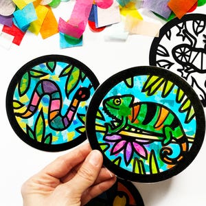 May include: Two round, black-framed stained glass art pieces. One features a green chameleon with orange stripes on a branch with pink and purple flowers. The other features a pink and purple snake on a green leaf background.
