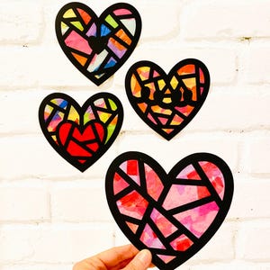 May include: Four heart-shaped decorations featuring black outlines and translucent, multi-colored segments. The hearts display various patterns of red, pink, yellow, orange, blue, and green colors, resembling stained glass art pieces.