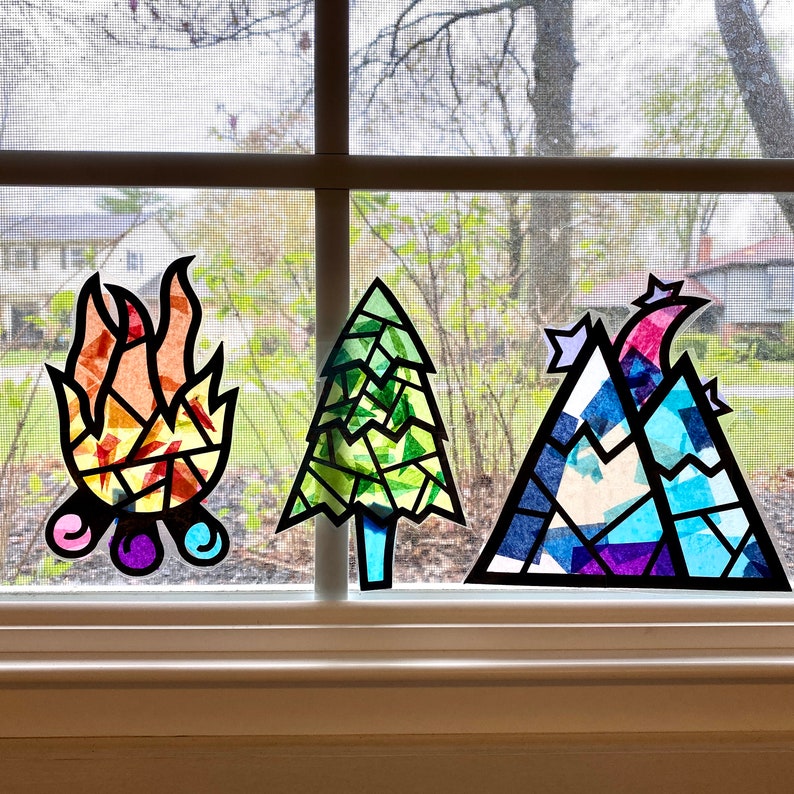 May include: Three stained glass window decorations, a campfire, a pine tree, and a mountain range. The decorations are made of colorful tissue paper and are perfect for adding a touch of whimsy to any window.