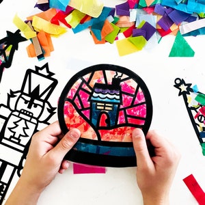 May include: A circular suncatcher craft featuring a black frame with a house design filled with translucent red, orange, yellow, green, blue, and purple tissue paper. The design includes a chimney and a roof, creating a stained glass effect.