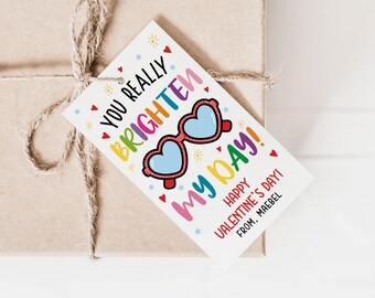 May include: A white Valentine's Day gift tag with colorful text that reads "You really brighten my day!" with a cartoon image of heart-shaped sunglasses. The tag also includes the text "Happy Valentine's Day! From, Mabel."