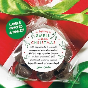 May include: A clear cellophane bag tied with a green ribbon, containing dark brown cubes. A circular label reads "It's beginning to SMELL a lot like CHRISTMAS." Instructions are printed below. A green circle with white text says "LABELS PRINTED & MAILED!"