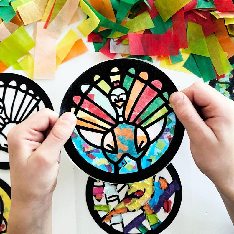 May include: A circular black paper frame featuring a cutout turkey design filled with translucent multicolored tissue paper pieces. The turkey has a fan-shaped tail with segments in yellow, orange, and red, and a body filled with blue and orange.