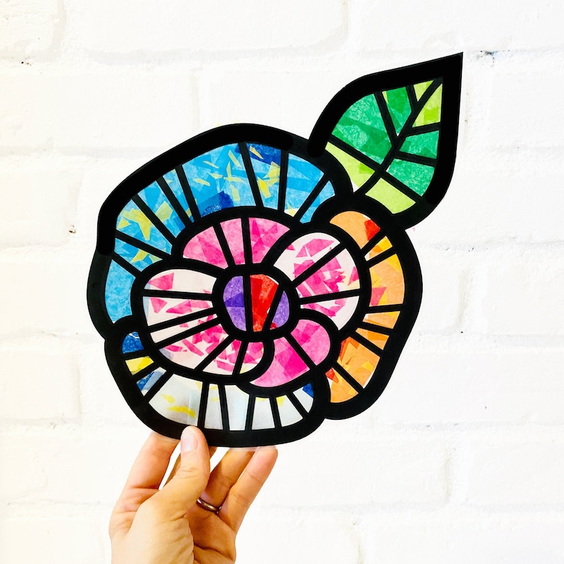 May include: A colourful paper flower with a black outline and a green leaf. The flower is made of different coloured paper squares that are layered on top of each other. The flower is a vibrant and cheerful piece of art.