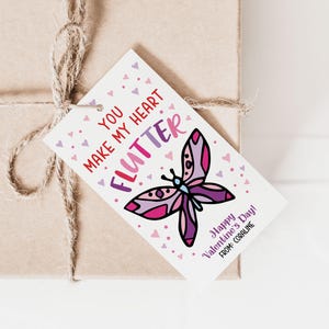 May include: A white gift tag with a pink and purple butterfly illustration. The text on the tag reads "You make my heart flutter" and "Happy Valentine's Day! From: Coraline".