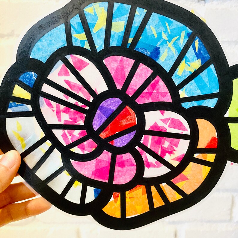 May include: A colourful stained glass style flower with pink, blue, yellow, red, and purple tissue paper. The flower is outlined in black and has a circular shape.
