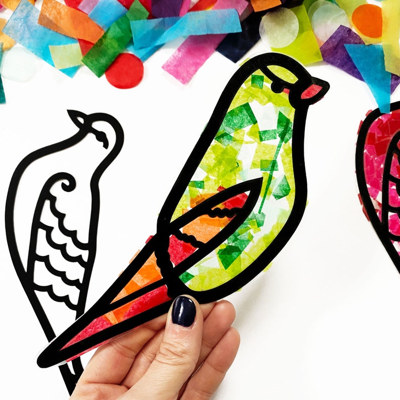 May include: A bird-shaped craft cutout with a thick black outline and a translucent body filled with small, colorful pieces of tissue paper in shades of green, yellow, orange, and red. A second, empty black outline of a bird is visible nearby.