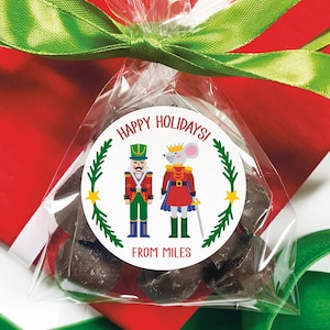May include: A clear cellophane bag filled with dark chocolate candies, tied with a green ribbon. A round sticker on the bag reads "Happy Holidays!" and features a nutcracker and a mouse king. The text "From Miles" is also on the sticker.