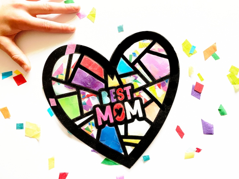 May include: A black heart-shaped frame filled with colorful tissue paper squares. The words "BEST MOM" are written in pink, red, and black letters inside the frame.